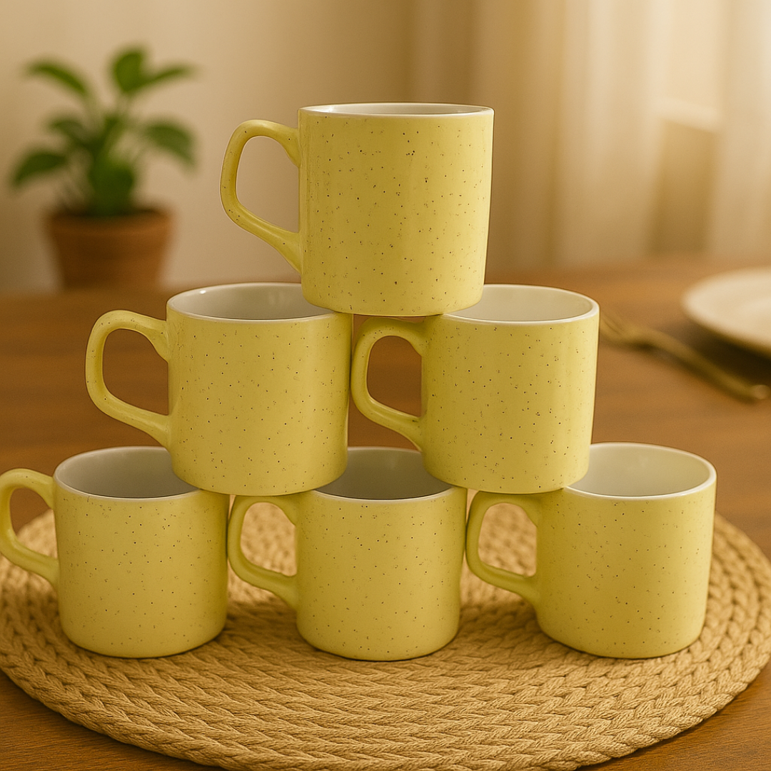 Set of 6 yellow speckled ceramic mugs stacked in a pyramid on a rope mat.