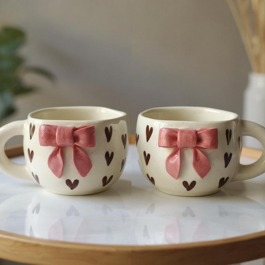IndoCasa handcrafted ceramic mugs with 3D pink bows and heart patterns, set of 2 placed on a round tray