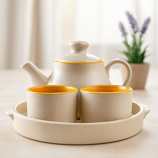 Elegant handcrafted ceramic tea set with teapot and two cups on a round tray, beige with mustard yellow interior, placed on a soft white ceramic dining table with lavender plant in background.