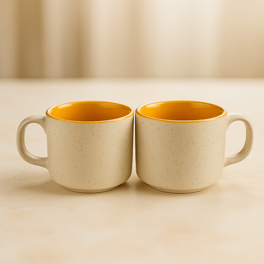 Two beige ceramic cups with mustard yellow interior and comfortable handles, placed side by side on a warm beige surface.