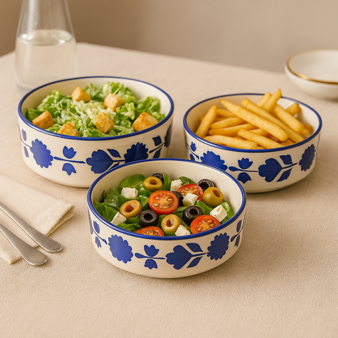 Three ceramic serving bowls filled with Caesar salad, French fries, and olive salad, styled on a dining table.